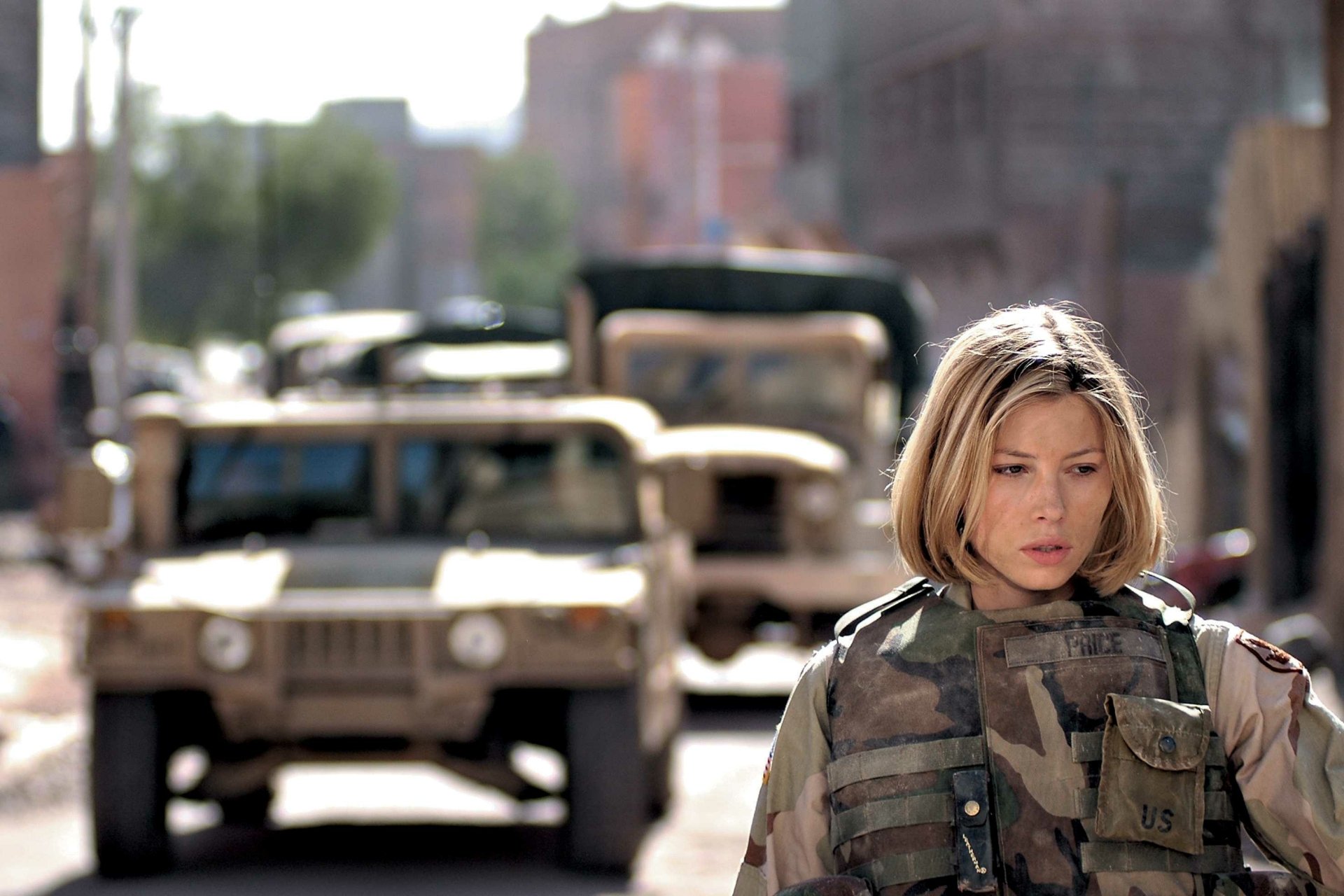 Female soldier from the movie Home of the Brave in camouflage, walking past military Humvees on a damaged city street — 2K Quad HD PC desktop wallpaper/background.
