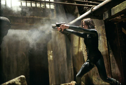 Kate Beckinsale wielding a gun in a dark, atmospheric scene from the movie Underworld, set in a gritty, industrial environment. HD PC desktop wallpaper and background.