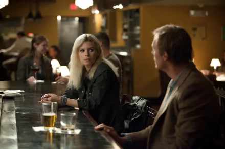 2K Quad HD PC desktop wallpaper: cinematic movie still of a blonde actress at a dimly lit bar, glancing toward a man seated at the counter.