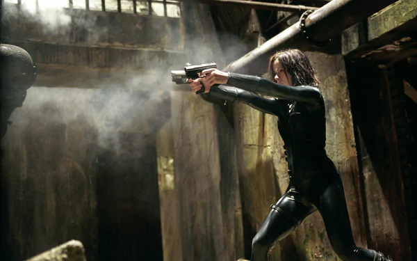 Kate Beckinsale wielding a gun in a dark, atmospheric scene from the movie Underworld, set in a gritty, industrial environment. HD PC desktop wallpaper and background.