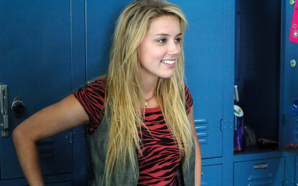 Amber Heard smiles in a scene from the movie Never Back Down, set against a backdrop of blue school lockers. This HD wallpaper captures her vibrant energy.