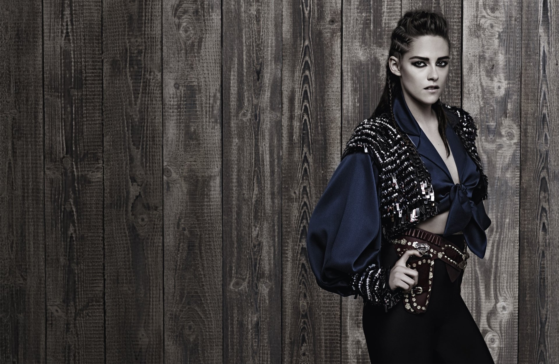 A striking 4K Ultra HD image featuring American actress Kristen Stewart, showcasing her black hair and a bold, fashionable look against a rustic wooden backdrop.