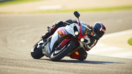 A Yamaha R1 motorcycle leans sharply into a turn on a racetrack, showcasing its sleek design and performance capabilities in this vibrant HD wallpaper.