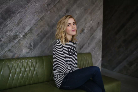 HD PC desktop wallpaper featuring celebrity Kiernan Shipka seated on a green leather couch against a textured gray wall background.