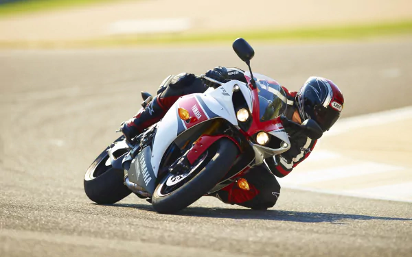 A Yamaha R1 motorcycle leans sharply into a turn on a racetrack, showcasing its sleek design and performance capabilities in this vibrant HD wallpaper.