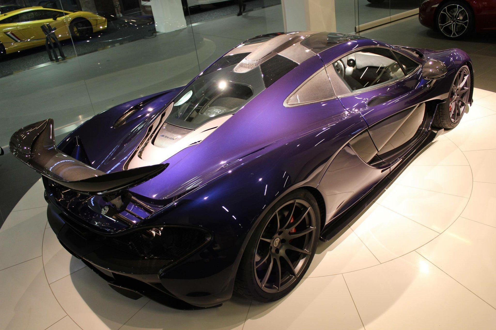 HD PC desktop wallpaper showcasing a sleek, dark purple McLaren P1 supercar in a showroom setting.