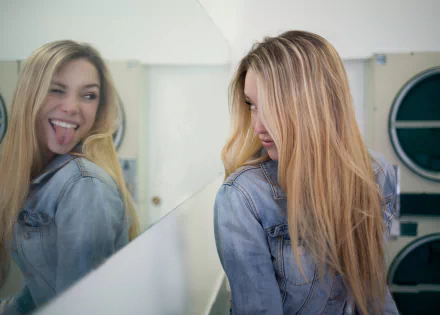 Blonde woman in a denim jacket playfully posing with her reflection, captured with mood and manipulation for a 4K Ultra HD PC desktop wallpaper.