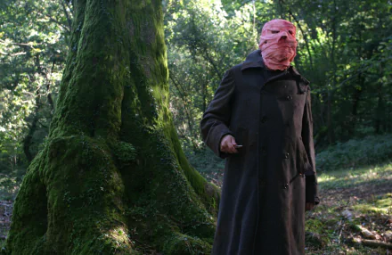 Timecrimes movie 2K Quad HD PC desktop wallpaper and background: masked man in a dark coat holding a knife in a mossy forest clearing.