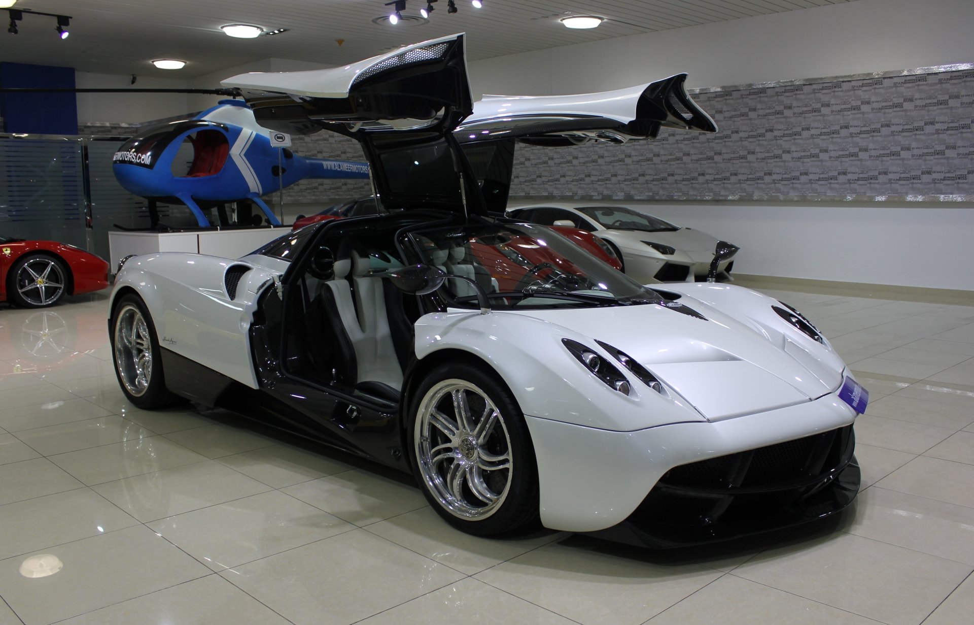 White Pagani Huayra sports car with butterfly doors open in a showroom, glossy floor reflection — 4K Ultra HD PC desktop wallpaper and background.