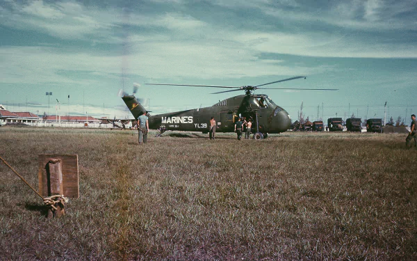 HD PC desktop wallpaper: military Sikorsky H-34 (Marines) parked on a grassy airfield with crew and support vehicles beneath a cloudy sky.