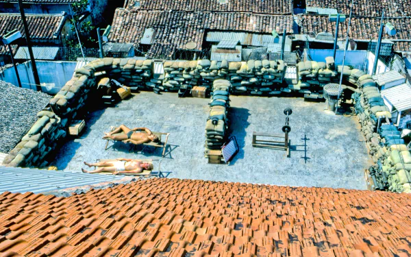HD desktop wallpaper depicting a military compound from the Vietnam War, featuring sandbag fortifications and soldiers resting inside the secured perimeter.