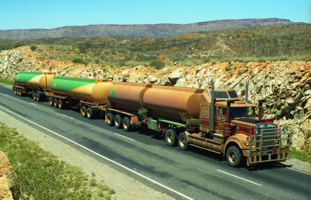 A Kenworth road train with multiple tanker trailers drives along a highway through a rocky, arid landscape, captured in a high-definition desktop wallpaper.