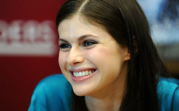 A bright and cheerful portrait of Alexandra Daddario, showcasing her joyful smile, set against a simple red background. This HD image serves as a striking desktop wallpaper.