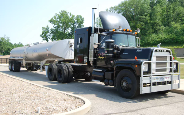 HD desktop wallpaper featuring a black Mack Trucks tanker vehicle parked on a road with greenery in the background.