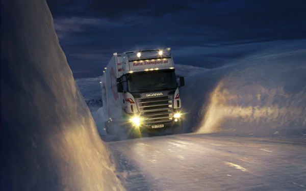 HD PC desktop wallpaper and background showing a Scania vehicle — heavy truck carving through deep snow at night, headlights cutting through drifting snow on an icy mountain road.