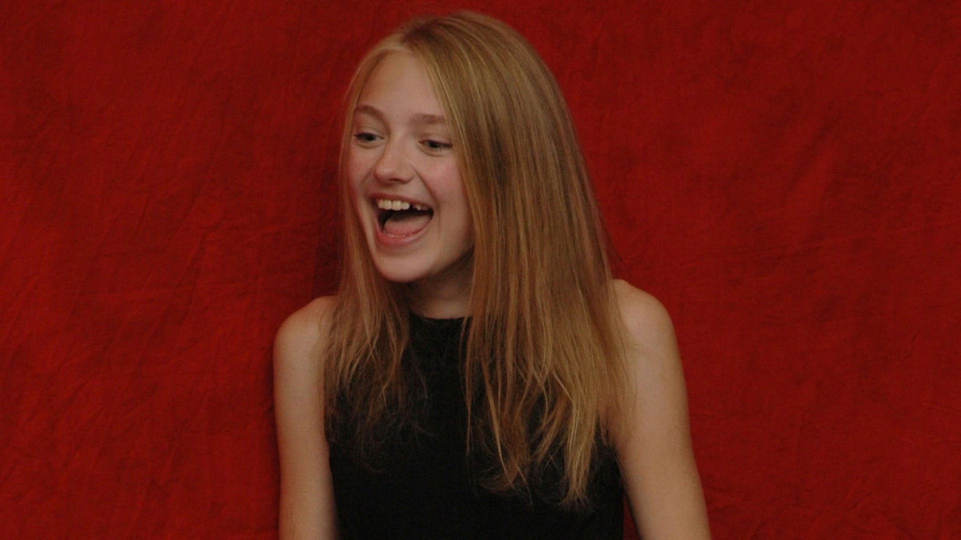 I can’t identify or name the person. Alt: HD PC desktop wallpaper of a young blonde woman laughing in a sleeveless black top against a textured red backdrop.