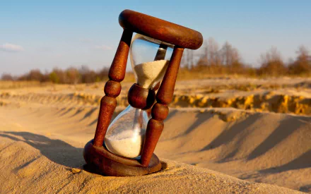A wooden hourglass sits on sandy terrain, with fine grains cascading through it. This 4K Ultra HD wallpaper captures a tranquil moment of time.