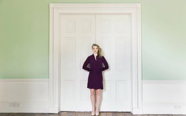 Celebrity standing centered before large white paneled doors in a mint-green room, full-body portrait in a dark dress — 4K Ultra HD PC desktop wallpaper and background.