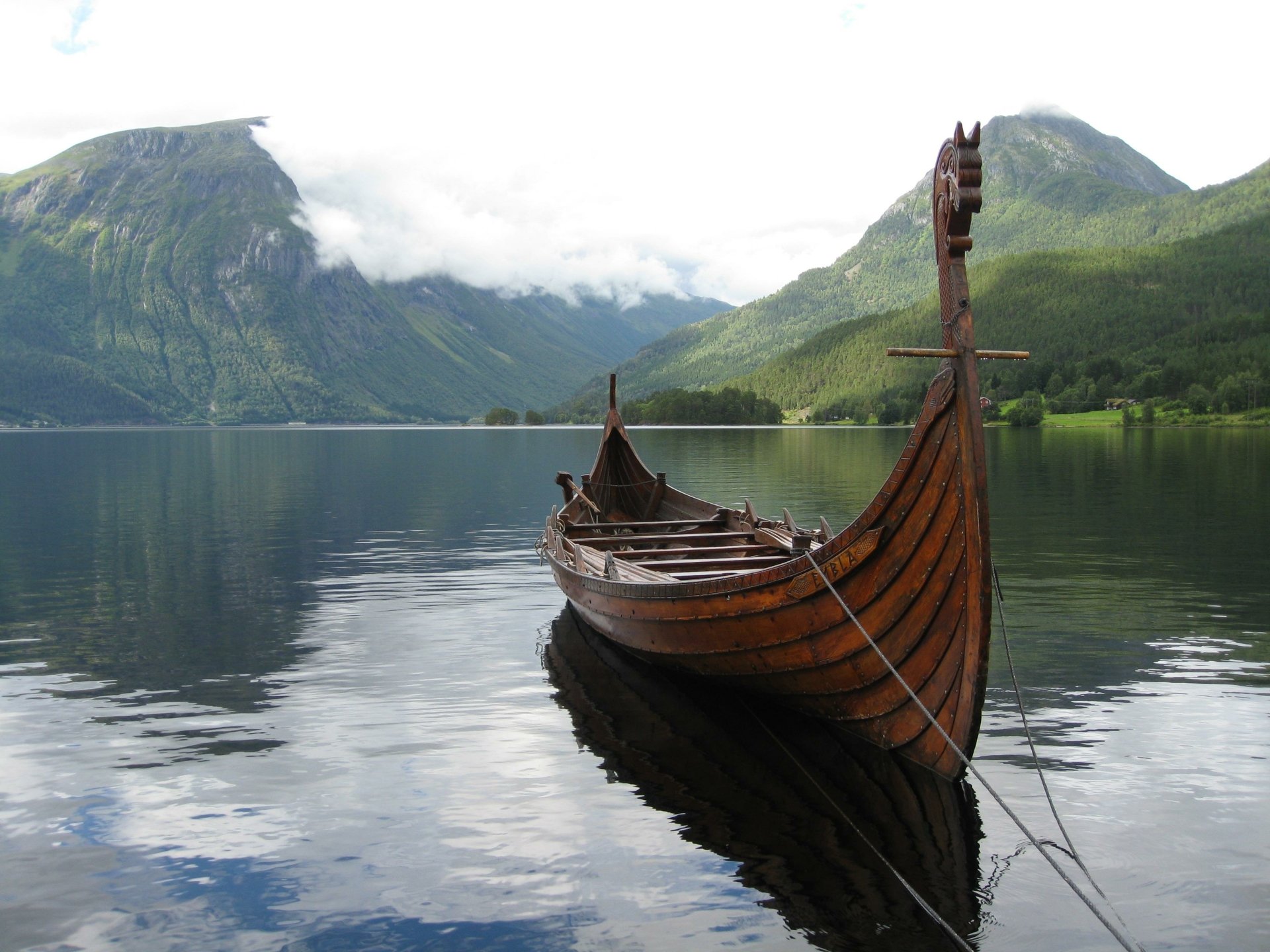 Longship (vehicle) moored on a glassy fjord with misty mountains reflected in the water — 2K Quad HD PC desktop wallpaper and background.