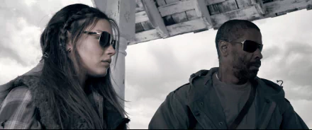 HD PC desktop wallpaper of two actors from The Book of Eli: a woman and a man in sunglasses beneath a weathered shelter, moody post-apocalyptic scene.