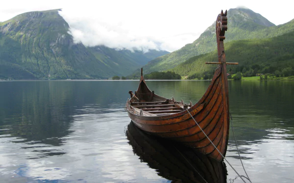 Longship (vehicle) moored on a glassy fjord with misty mountains reflected in the water — 2K Quad HD PC desktop wallpaper and background.