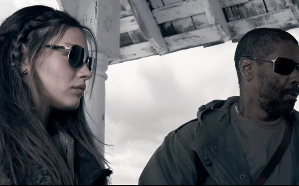 HD PC desktop wallpaper of two actors from The Book of Eli: a woman and a man in sunglasses beneath a weathered shelter, moody post-apocalyptic scene.