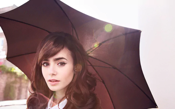 HD PC desktop wallpaper featuring celebrity Lily Collins holding a dark umbrella, with soft natural lighting and a blurred outdoor background.