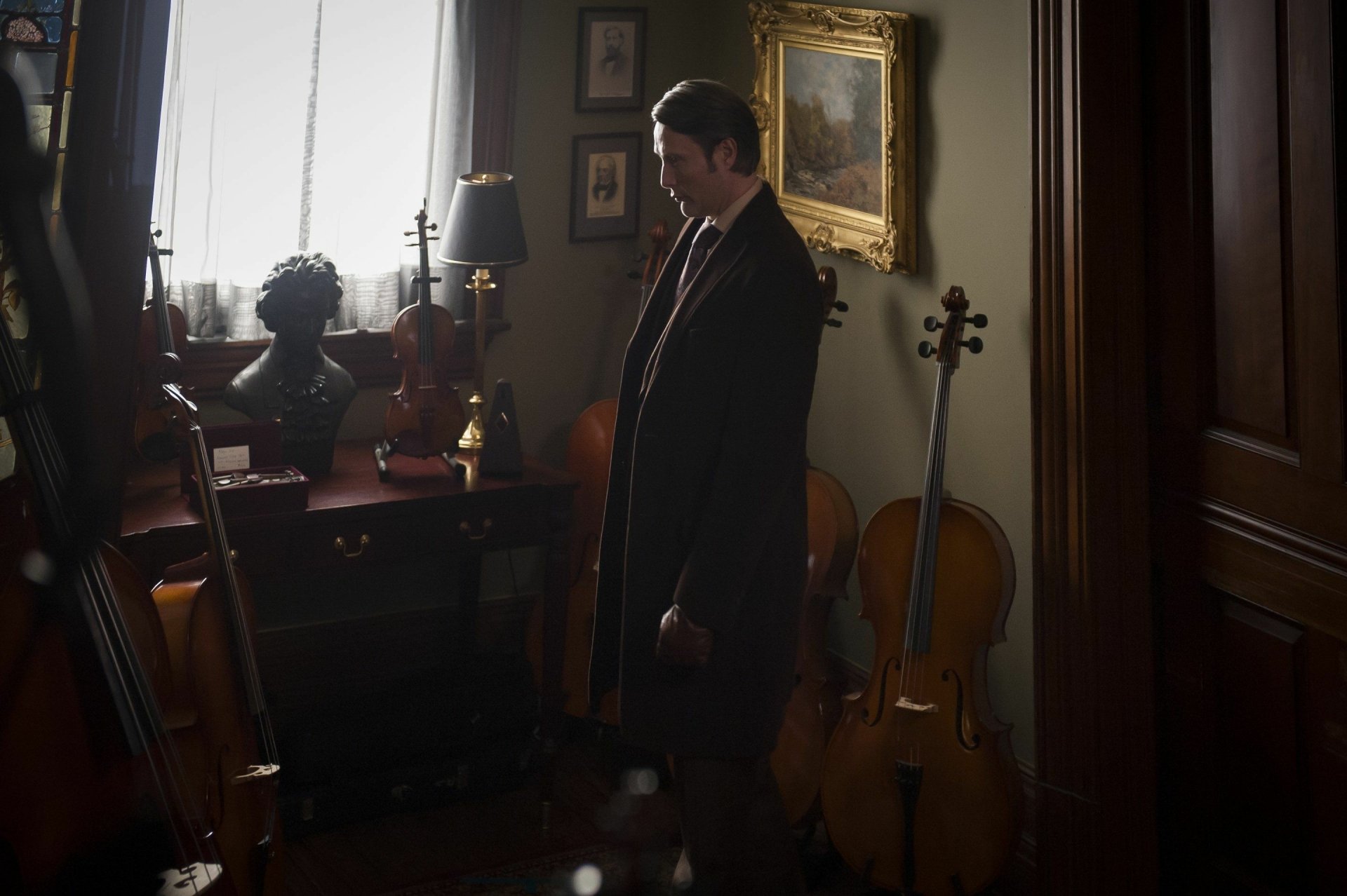 Brooding man in a dim instrument-filled parlor, cinematic TV-show scene — moody 2K Quad HD PC desktop wallpaper evoking Hannibal.
