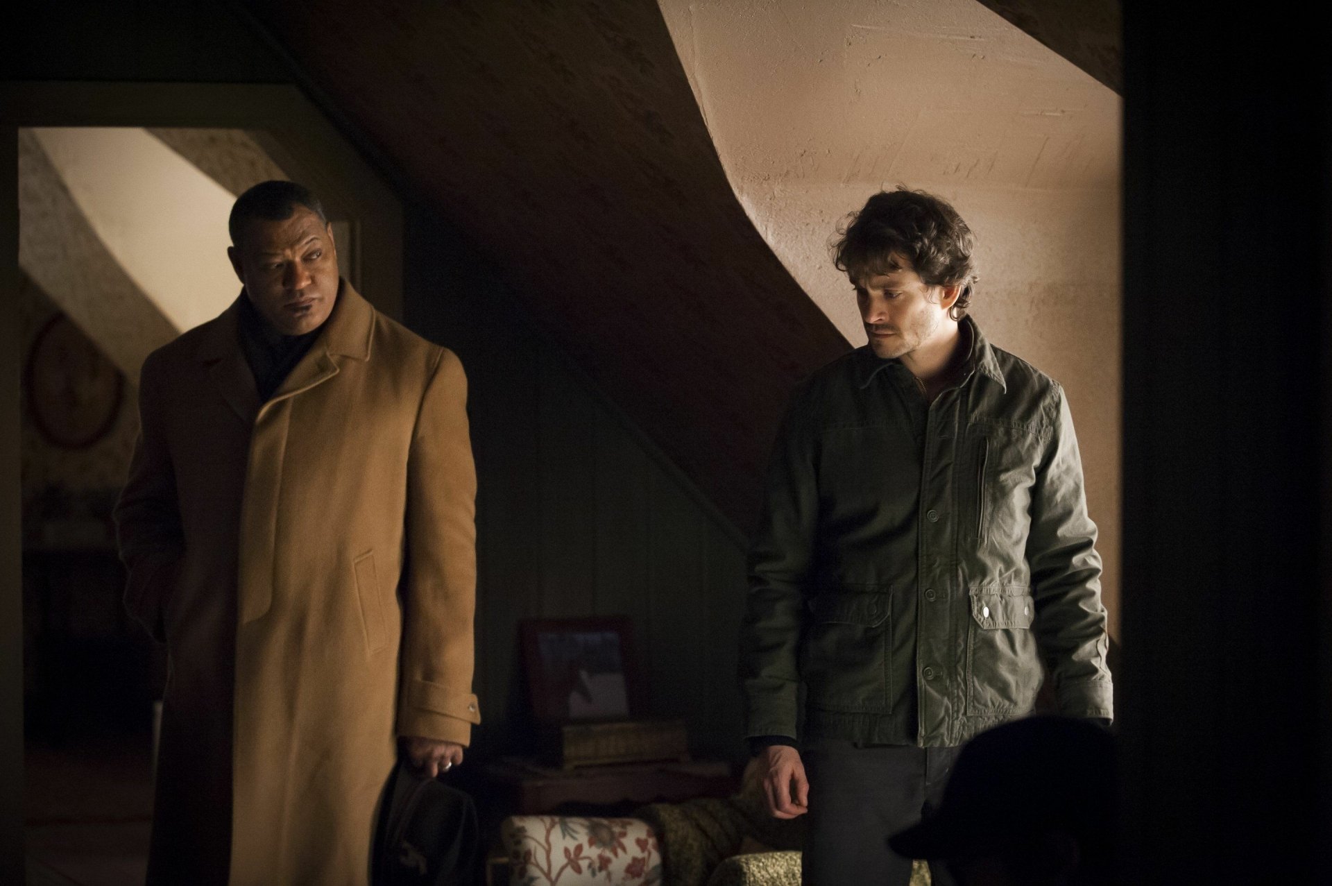 Moody Hannibal TV show scene: two men in a dim attic, one in a tan coat and one in a dark jacket sharing a tense glance — 2K Quad HD PC desktop wallpaper/background.