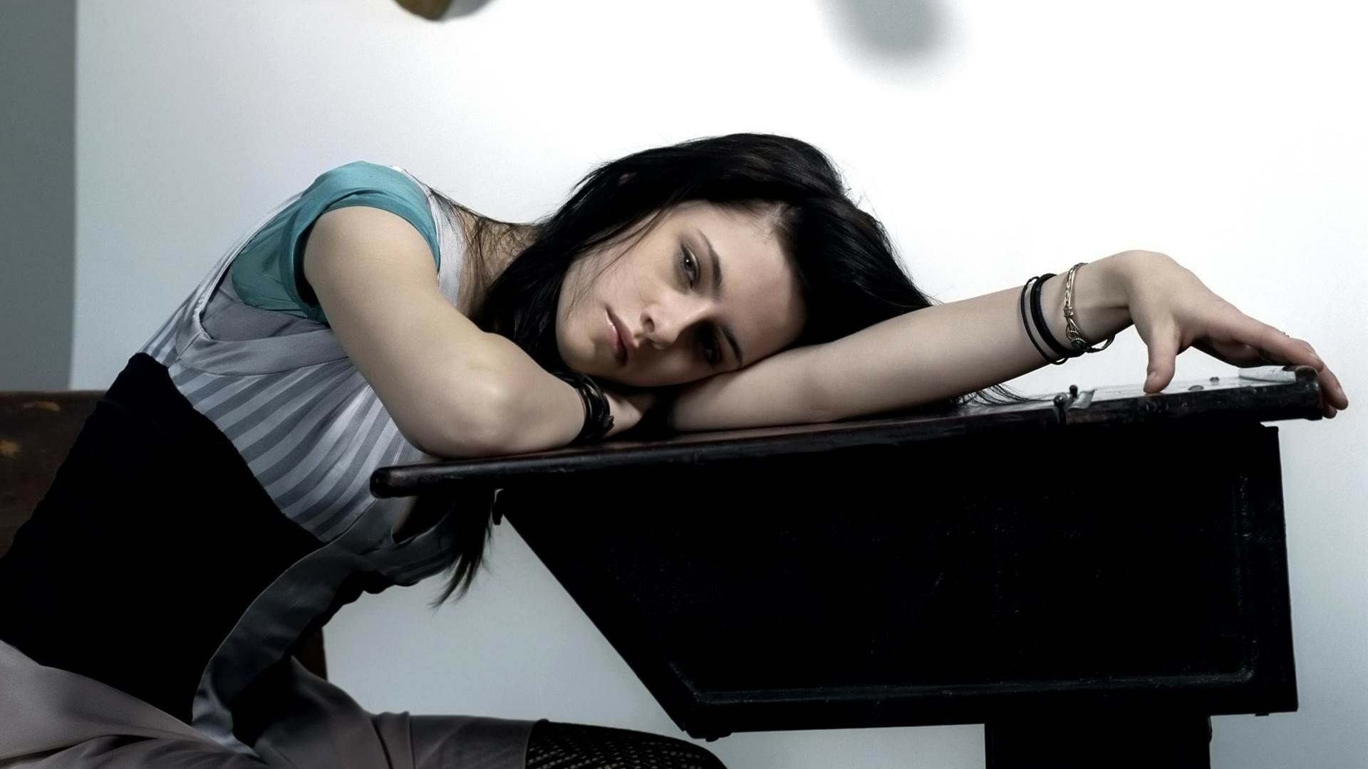 HD PC desktop wallpaper featuring celebrity Kristen Stewart resting her head on a piano, with a contemplative expression against a simple, light background.