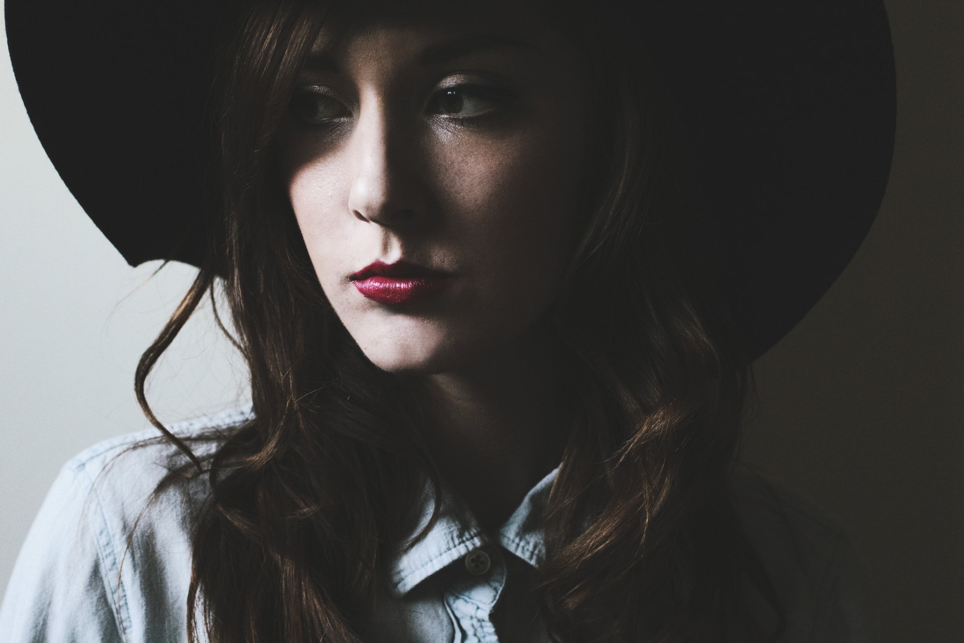 HD desktop wallpaper of a brunette woman with brown eyes wearing a hat and red lipstick, captured in soft lighting with a contemplative expression.