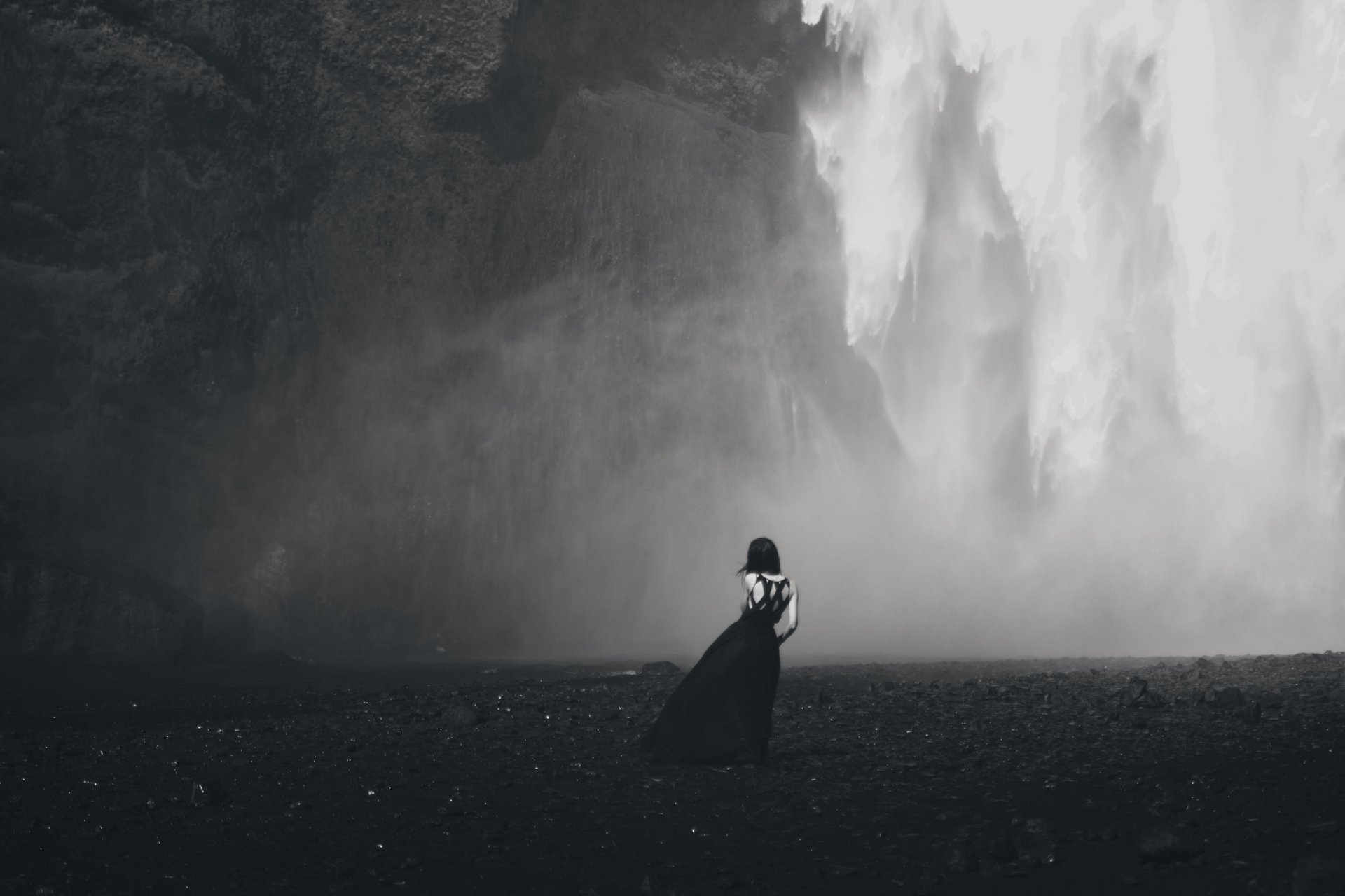 Black and white HD wallpaper showing a woman from the rear standing in front of a dramatic waterfall, creating a striking landscape background.