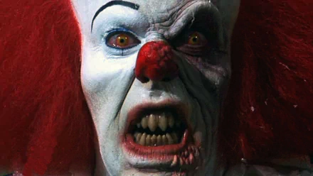 HD desktop wallpaper of Pennywise, the menacing clown from the 1990 movie It, displaying an unsettling expression with yellow eyes and sharp teeth.