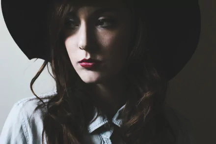HD desktop wallpaper of a brunette woman with brown eyes wearing a hat and red lipstick, captured in soft lighting with a contemplative expression.