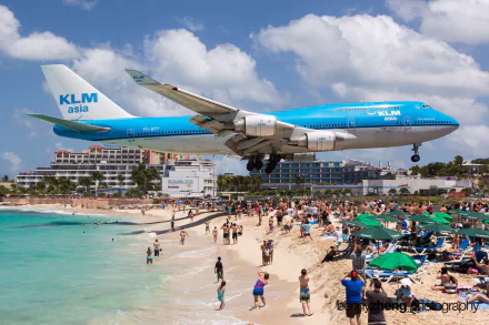 A Boeing 747 approaches Maho Beach in Saint Martin, flying low over sunbathers and umbrellas, showcasing the vibrant beach atmosphere against a clear blue sky.