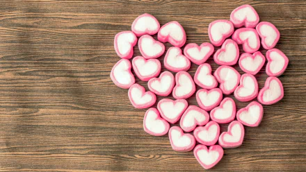 A collection of pink and white heart-shaped marshmallows arranged to form a heart on a wooden background, embodying romantic love and sweet confectionery delight. 4K Ultra HD quality.