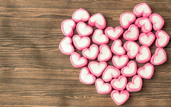 A collection of pink and white heart-shaped marshmallows arranged to form a heart on a wooden background, embodying romantic love and sweet confectionery delight. 4K Ultra HD quality.