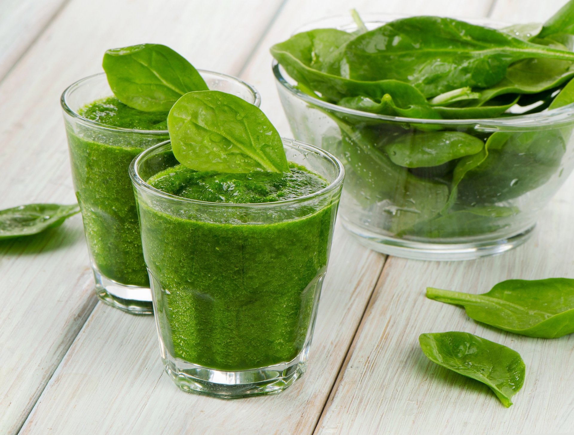 Close-up of green vegetable smoothie with fresh spinach leaves, set against a bright wooden background, captured in 4K Ultra HD for PC desktop wallpaper.