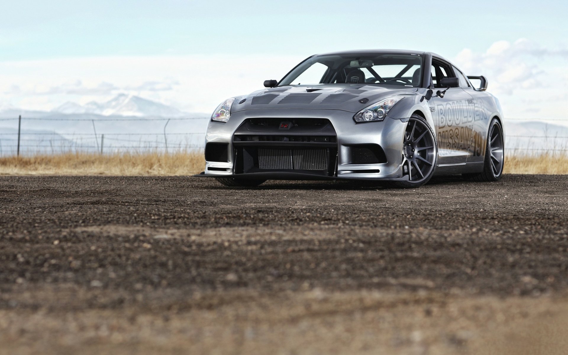 A sleek Nissan GT-R stands on an open terrain, showcasing its powerful design against a backdrop of distant mountains, captured in high-definition for a stunning desktop wallpaper.