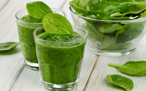 Close-up of green vegetable smoothie with fresh spinach leaves, set against a bright wooden background, captured in 4K Ultra HD for PC desktop wallpaper.