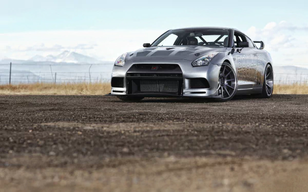 A sleek Nissan GT-R stands on an open terrain, showcasing its powerful design against a backdrop of distant mountains, captured in high-definition for a stunning desktop wallpaper.