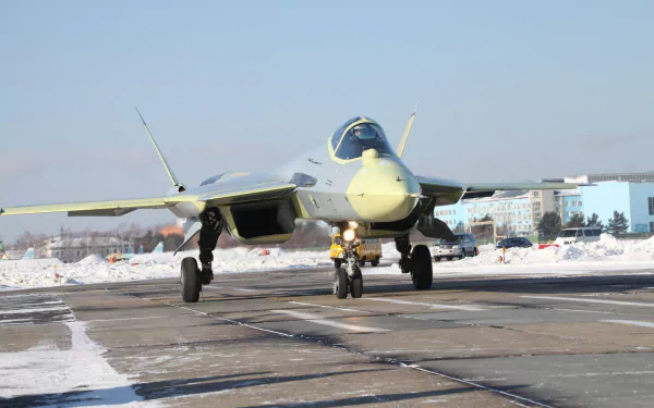 A Sukhoi Su-57 military jet taxis on a snowy runway, showcasing its advanced design and capabilities in this HD desktop wallpaper.