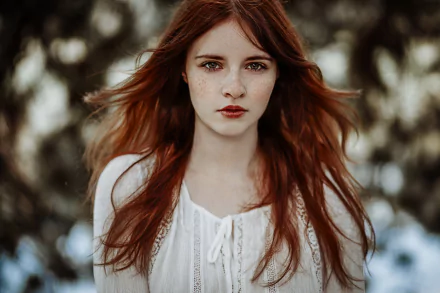 A striking redhead with brown eyes and freckles gazes directly at the viewer, surrounded by a soft bokeh background, creating a captivating portrait.