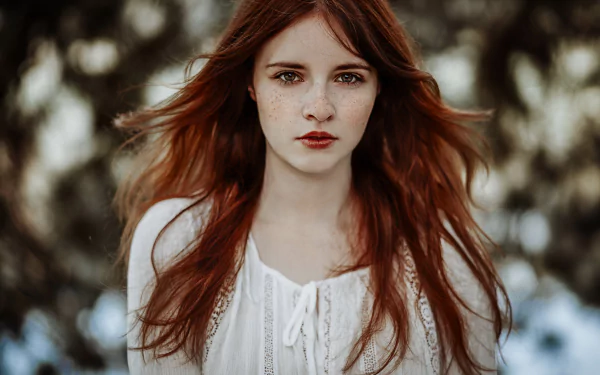A striking redhead with brown eyes and freckles gazes directly at the viewer, surrounded by a soft bokeh background, creating a captivating portrait.