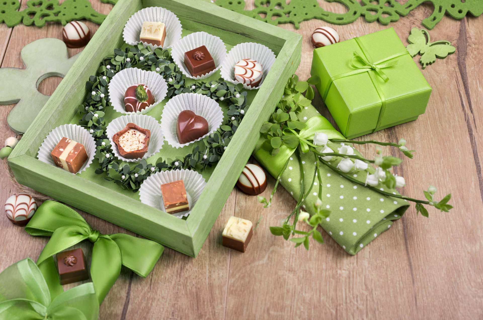 A vibrant display of assorted chocolates in a green box, surrounded by decorative elements like ribbons and a gift, creating a delightful sweets-themed wallpaper for desktops.