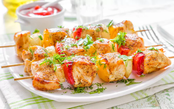 Close-up of grilled meat and vegetable kebabs garnished with fresh herbs on a white plate, presented as a vibrant 4K Ultra HD food and barbecue desktop wallpaper.