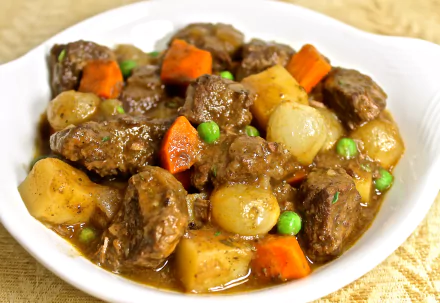 4K Ultra HD PC desktop wallpaper of hearty beef stew — chunks of beef, potatoes, pearl onions, carrots and peas in rich gravy on a white plate.