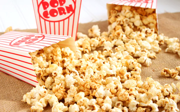 Two striped popcorn containers spill popcorn onto a textured surface in this vibrant 4K Ultra HD wallpaper. Enjoy the appetizing visual feast of this classic snack.