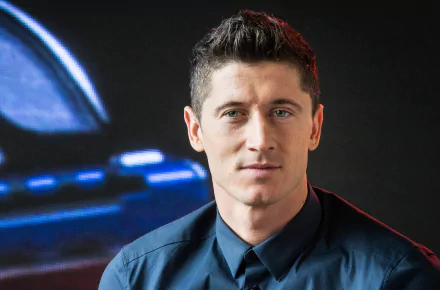 High-definition desktop wallpaper featuring Polish soccer player Robert Lewandowski in a blue shirt, captured against a dark background with a blurred blue and red light.