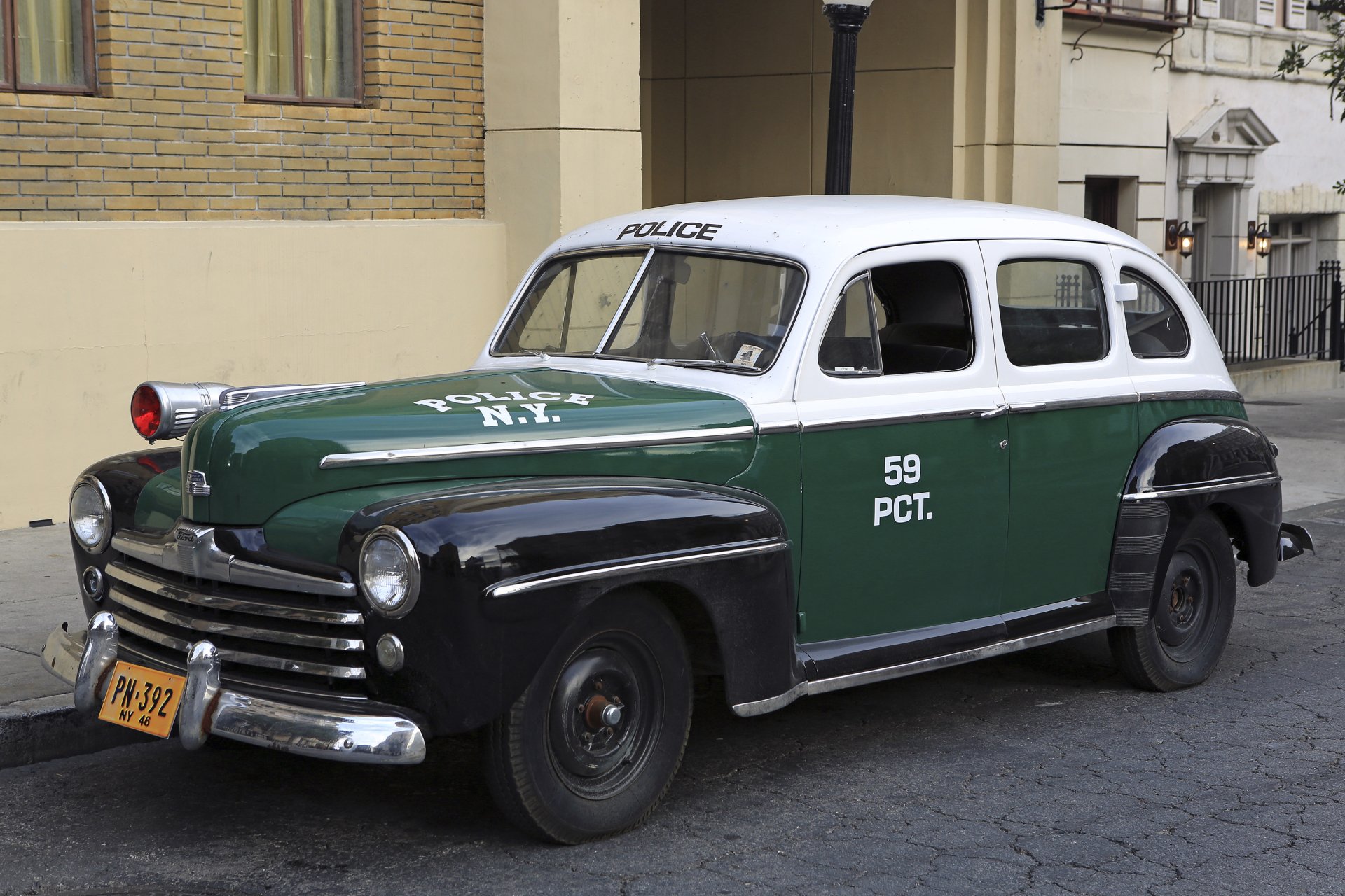 HD PC desktop wallpaper featuring a classic Ford police vehicle in green, black, and white parked on a city street, showcasing vintage law enforcement design.